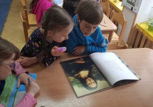 Dwoje dzieci ogląda album z Mona Lisą. Dziewczynka siedząca obok nich koloruje